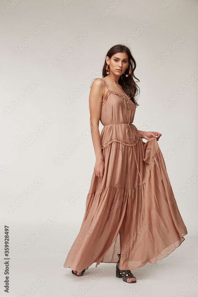 Beautiful woman fashion model makeup brunette hair perfect body shape tanned skin wear clothes summer collection organic long beige silk dress stylish sandals shoes, accessory jewelry earrings date. Beautiful woman fashion model makeup brunette hair perfect body shape tanned skin wear clothes summer collection organic long beige silk dress stylish sandals shoes, accessory jewelry earrings date.