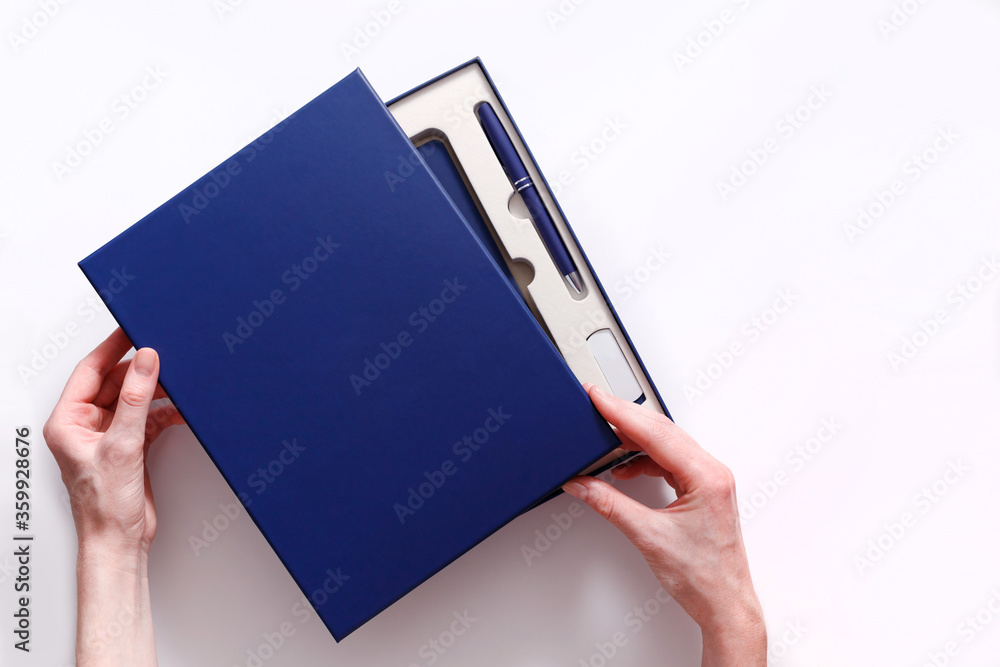 Woman hands open cover of corporate style box with pen, flash drive and notebook isolated on white background. View from above