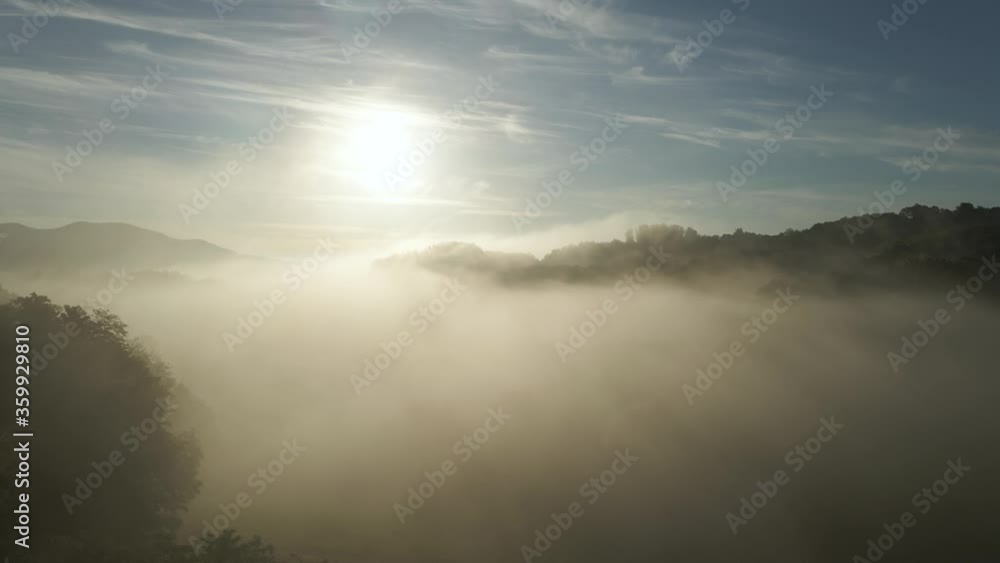 Drone flying over the ground fog and mist covering the hilltops and mountains with bright sun shining over them. Aerial. Drone flying over the ground fog and mist covering the hilltops and mountains with bright sun shining over them. Aerial.