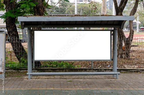 The empty blank white mock up billboard at the bus stop in the city park. In mock up billboard for ads, advertising, maps of buses and street next to road.