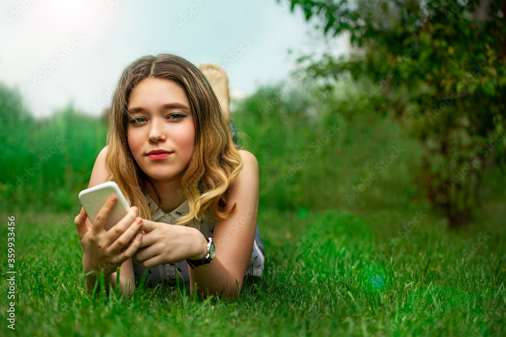 beautiful girl lies on green grass with a smartphone in her hands in the park beautiful girl lies on green grass with a smartphone in her hands in the park