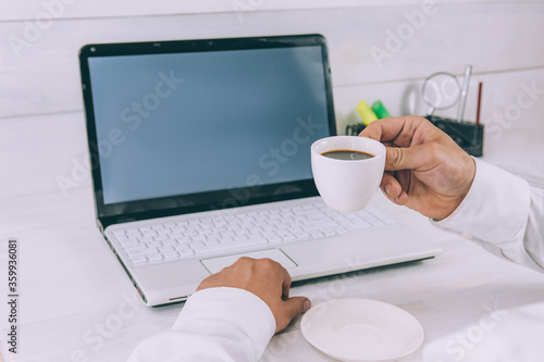 Mock-up Technology. Businessman holds a smartphone in his hands  on a background of laptop and coffee on a wooden table.