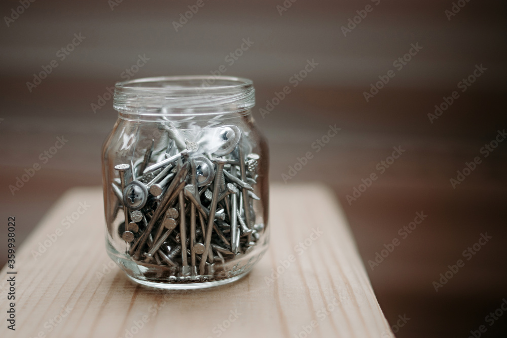Close up glass jar with metal screws on wood, bokeh background selective and soft focus. Iron nails. Copy space
