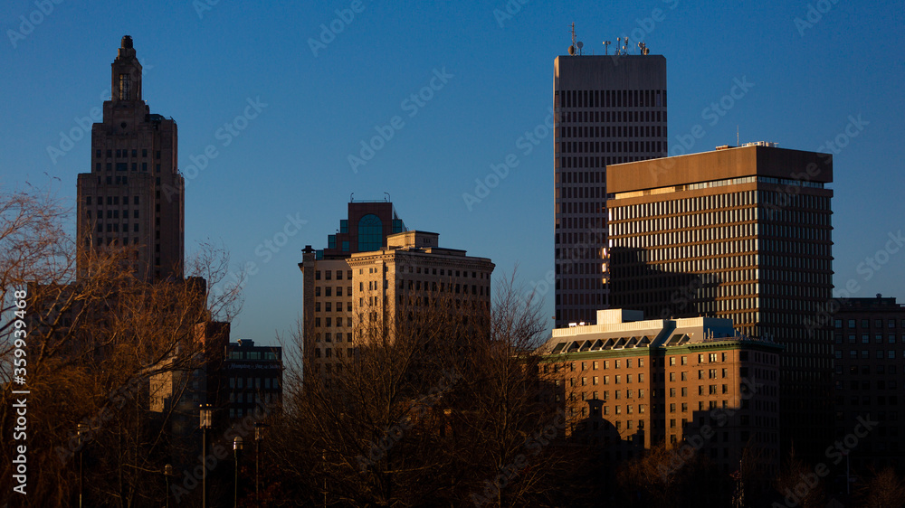view from a distance of the downtown providence, rhode island skyline that is lit up with a touch of gold by a setting sun