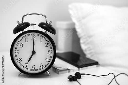 Alarm clock on table with mobile phone, notebooks and headphone. Wake up concept. An image of a alarm clock showing 07:00 am. photo