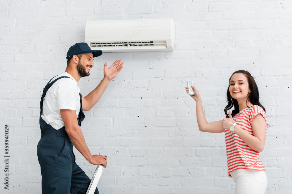 Side view of smiling woman with remote controller of air conditioner