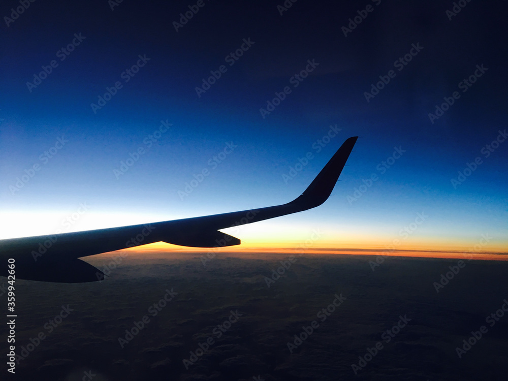 Obraz premium 飛行機の窓から見たカラフルな空と飛行機の翼のシルエット
