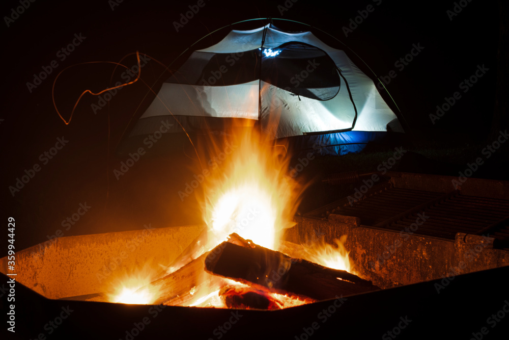 Blazing campfire in front of an illuminated tent at night. Blazing campfire in front of an illuminated tent at night.