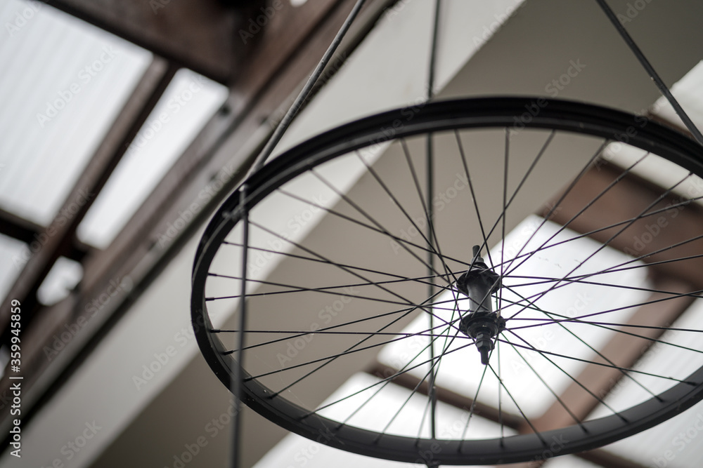 A Bicycle wheel is using to decorate the ceiling of retro or loft style building by hanging down with cable rope, interior design object photo. Close-up and selective focus.