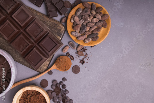 Chocolate pieces and drops, cocoa beans and powder on grey background