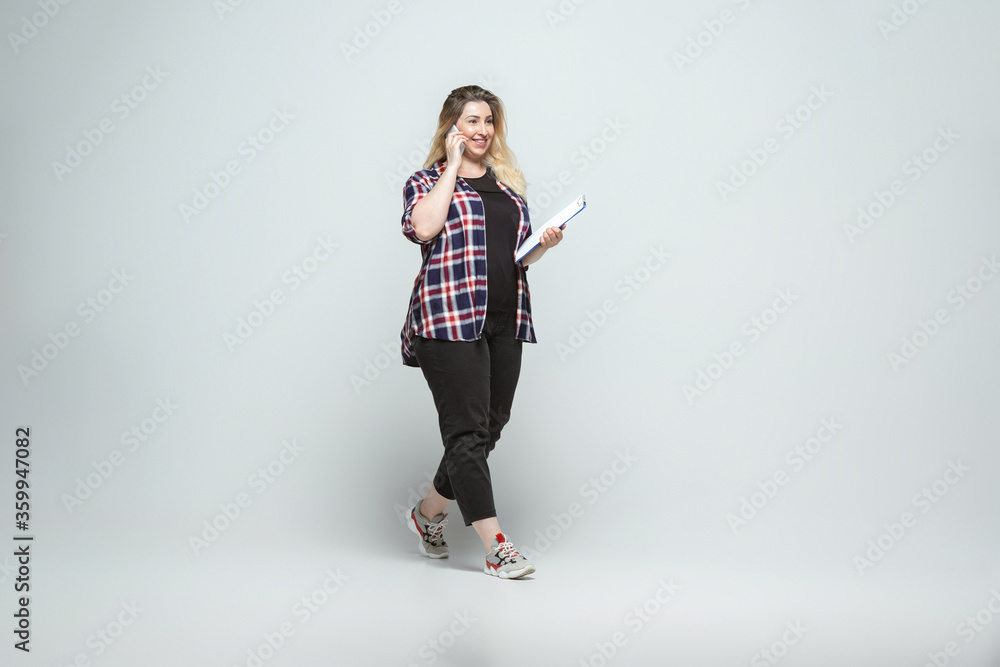 Devices, gadgets. Young woman in casual wear on gray background. Bodypositive character, feminism, loving herself, beauty concept. Plus size businesswoman, beautiful girl. Inclusion, diversity. Devices, gadgets. Young woman in casual wear on gray background. Bodypositive character, feminism, loving herself, beauty concept. Plus size businesswoman, beautiful girl. Inclusion, diversity.