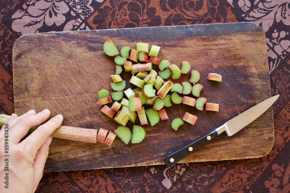 Flat lay image of cutting rhubarb stalks on teak cutting board