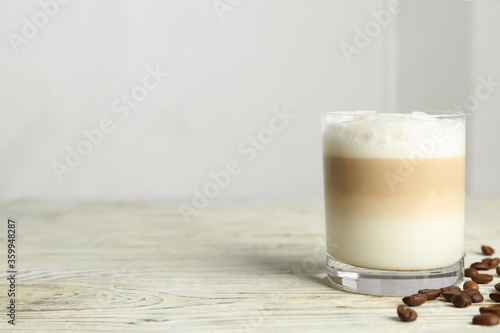 Delicious latte macchiato and coffee beans on white wooden table indoors, space for text
