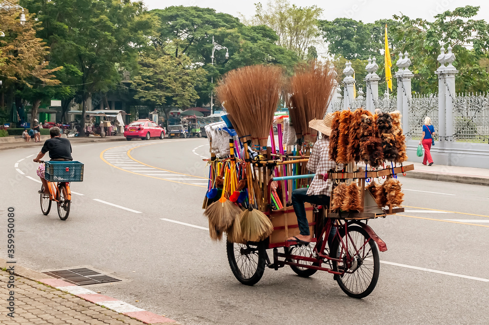 Street vendor of brooms and feather dusters travels a street in central Bangkok, Thailand, with the rickshaw full of goods