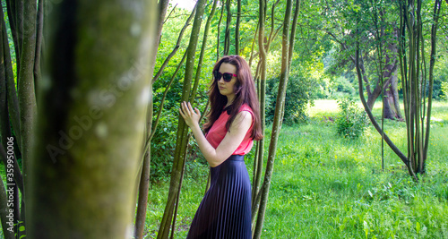 Young girl in sunglasses behind tree trunks. Concept image.