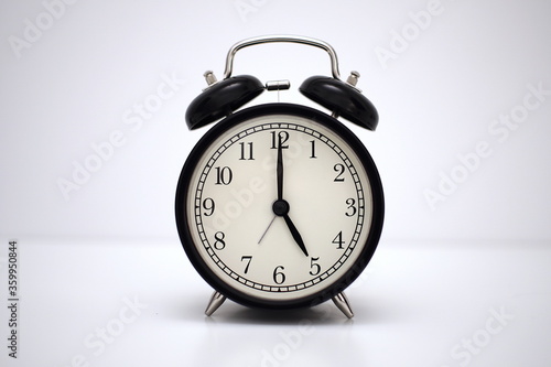 Black vintage alarm clock on table. White background. Wake up concept. An image of a retro clock showing 05:00 pm/am. 