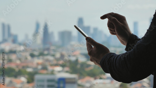 A man dials a message on a smartphone against the background of the panorama of the city of Jakarta. Accelerated video.