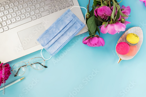 Flat lay composition with medical mask lyin on the laptop, coffee and peonies on blue background. photo