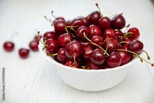 ripe cherries in a white plate on a white wooden background. Vegetarian concept, food.
