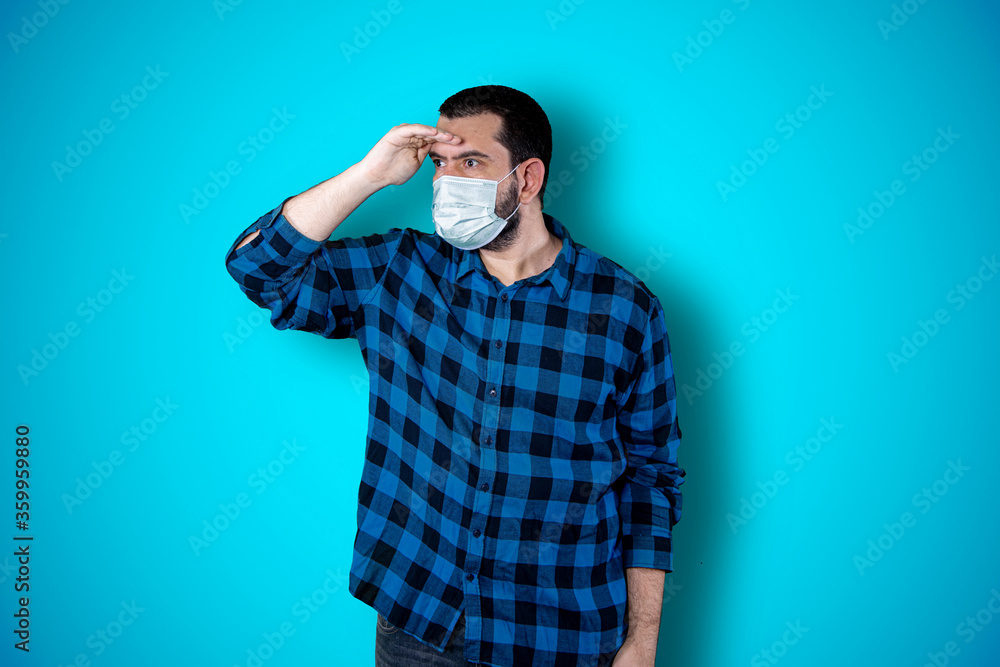 Young man using mask pointing and looking at copy space. Handsome young businessman isolated on blue background. Coronavirus concept Young man using mask pointing and looking at copy space. Handsome young businessman isolated on blue background. Coronavirus concept