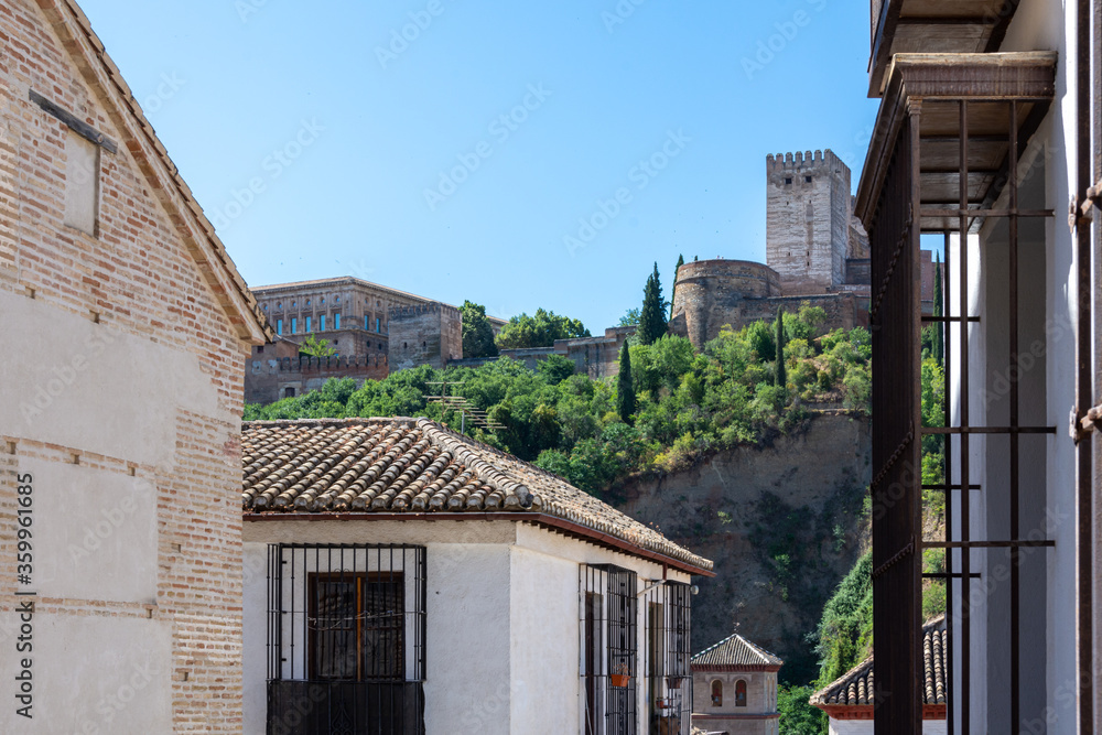 Narrow streets of the Granada neighborhood of Albaicín with the towers of the Alcazaba of the Alhambra in the background