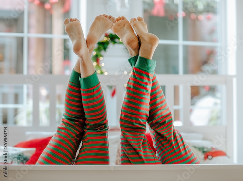 Man's and woman's barefooted legs up in red and green stripped Christmas pyjamas in white room.