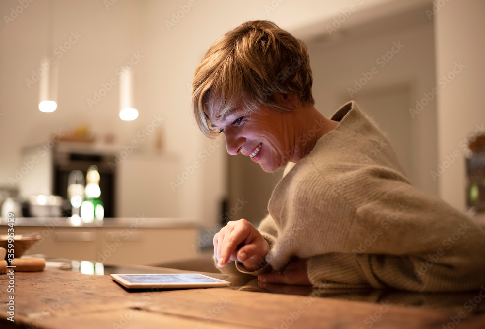 Smiling woman working late while using digital tablet in illuminated living room Smiling woman working late while using digital tablet in illuminated living room