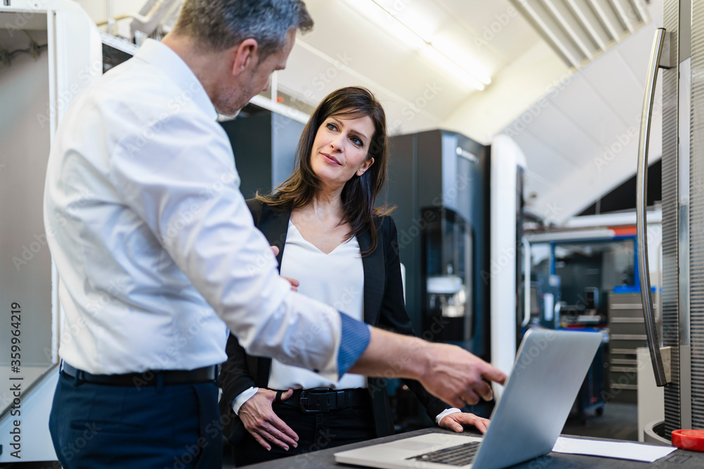 Businessman and businesswoman with laptop having a work meeting in a factory Businessman and businesswoman with laptop having a work meeting in a factory