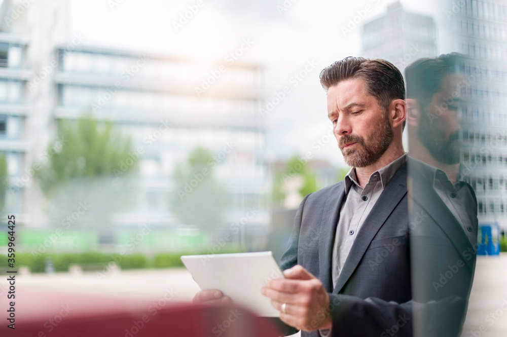 Confident businessman using digital tablet while standing outside office building in city Confident businessman using digital tablet while standing outside office building in city