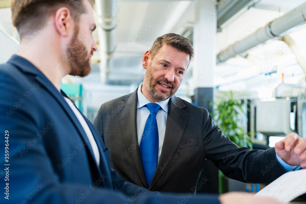 Two businessmen having a work meeting in a factory discussing a plan Two businessmen having a work meeting in a factory discussing a plan