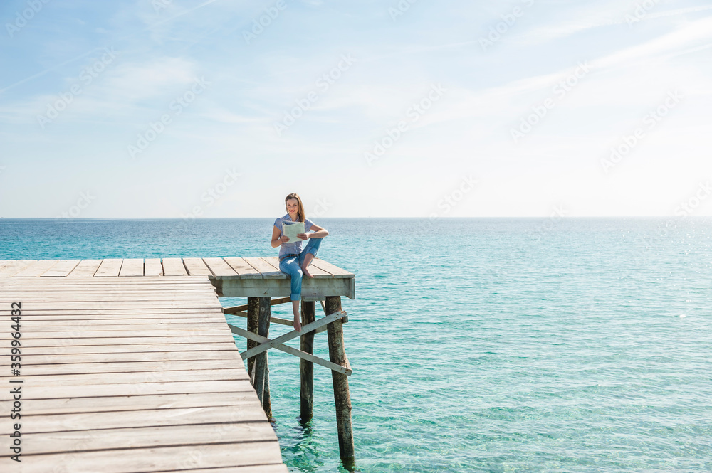 Woman sitting on jetty reading magazine, Mallorca, Spain Woman sitting on jetty reading magazine, Mallorca, Spain