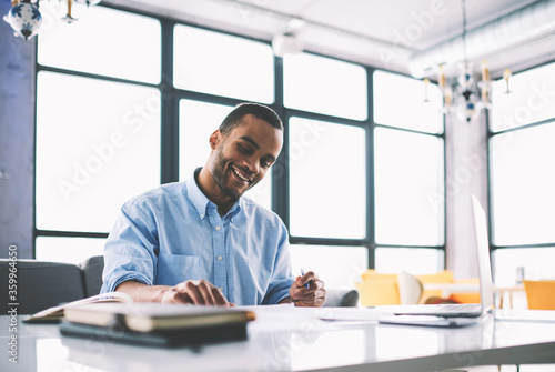 Afro american graphic designer satisfied with creating plan for successful project writing notes in cabinet, smiling dark skinned student enjoying working on creative homework task preparing report