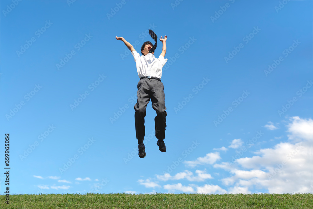 青空を背景にジャンプをする男子高校生