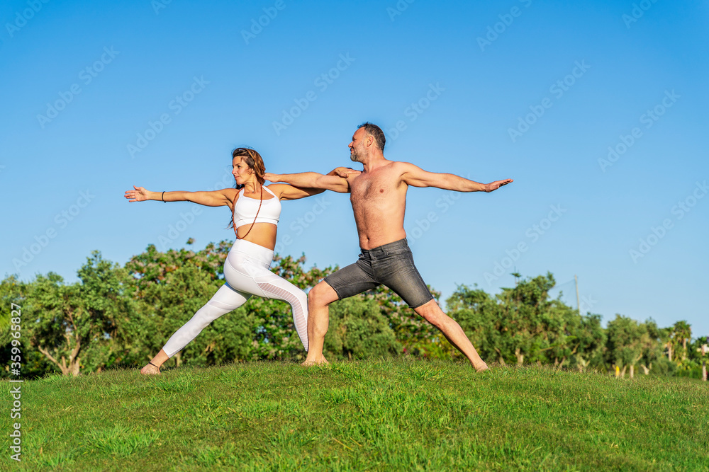 Mature couple doing yoga on lawn in sunshine together Mature couple doing yoga on lawn in sunshine together