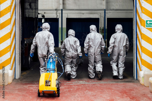 Rear view of sanitation coworkers entering warehouse with decontamination chemical