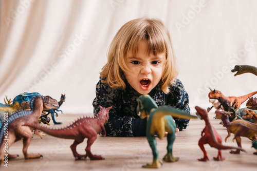 Portrait of little girl lying on the floor playing with toy dinosaurs photo