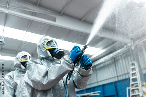 Low angle view of sanitation workers spraying chemical from hose in warehouse photo