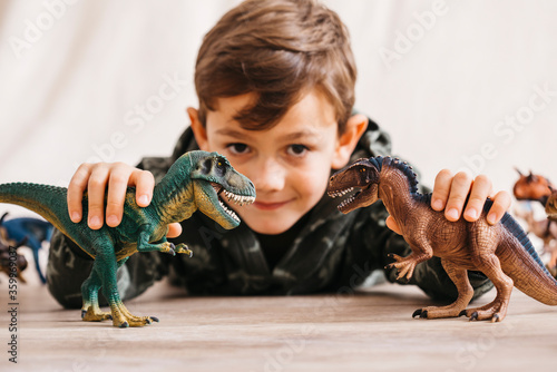 Smiling little boy lying on the floor playing with toy dinosaurs photo