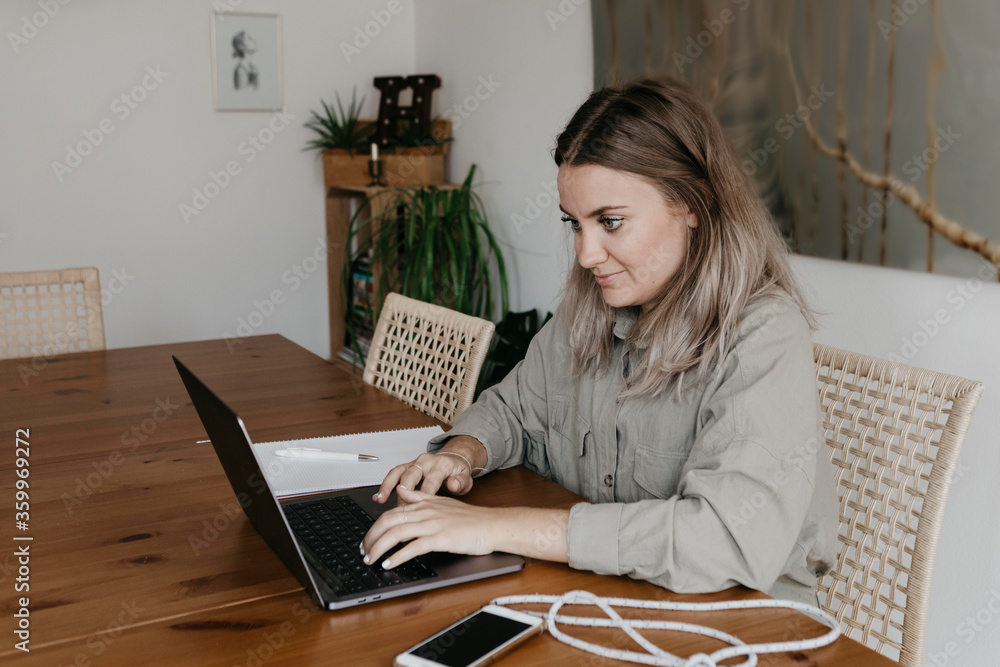 Woman using laptop while sitting at table in dining room during home quarantine Woman using laptop while sitting at table in dining room during home quarantine