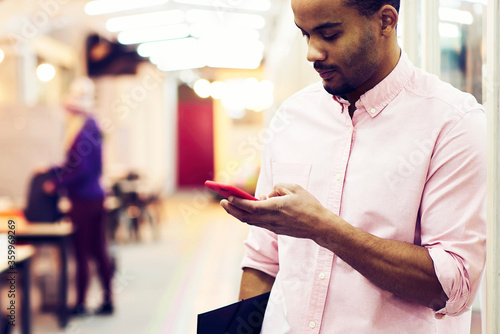 Young male journalist doing remote job being in business trip sending his publications and information to editor's email box via modern smartphone connected to fast wireless connection in coworking photo