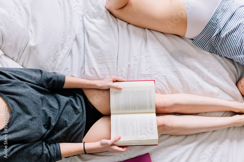 Crop viwe of two women wearing underwear lying on bed with a book photo