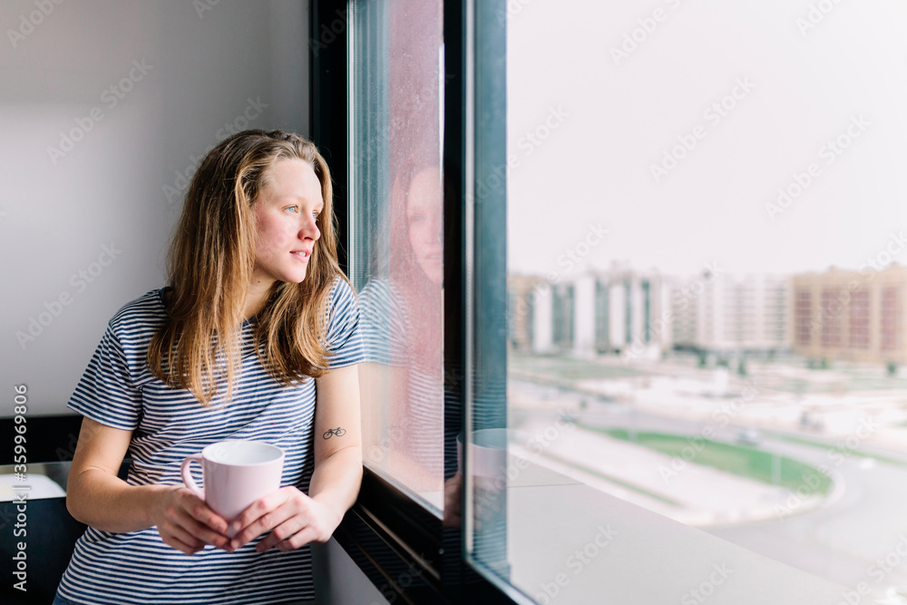 Portrait of young woman with mug looking out of window Portrait of young woman with mug looking out of window