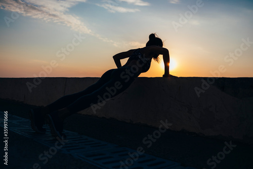 Full length of silhouette female athlete doing push-ups at promenade during sunrise