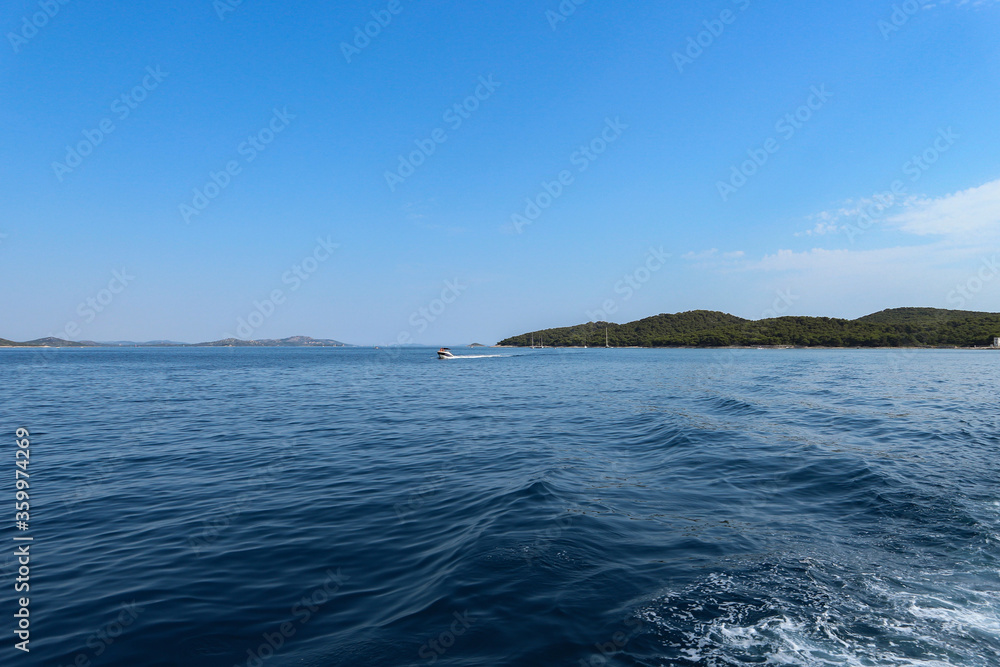 Sailing in open waters of Croatian Adriatic sea, leaving Vrgada island in the distance and boat wakes behind Sailing in open waters of Croatian Adriatic sea, leaving Vrgada island in the distance and boat wakes behind