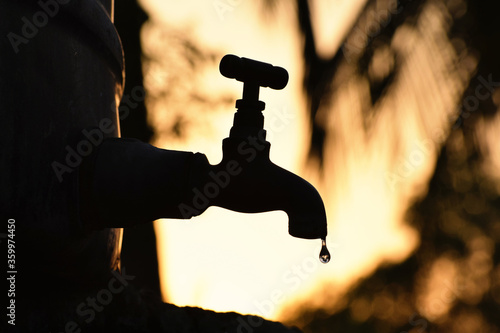 Silhouette of old vintage metal tap leaking last water droplet. alone in outdoor natural environment during the golden hour of sunrise, water shortage, crisis, scarcity 