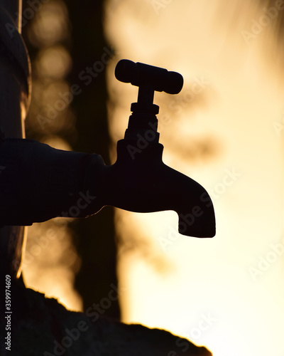 vertical / portrait-oriented Silhouette of old vintage metal tap alone in an outdoor natural dry environment during golden hour, water shortage 