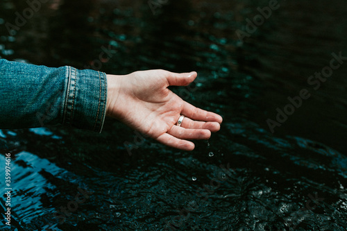 Germany, Young woman wetting hand in pond