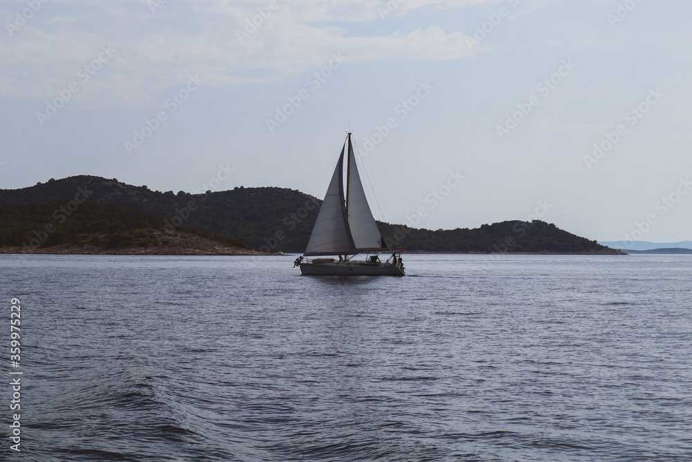 Sailboat with open sails, catching wind and passing by on the open sea in front of Vrgada island in central Dalmatia, Croatia