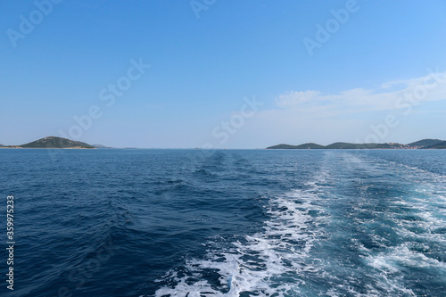 Sailing out on the open sea with Vrgada island in the distance and leaving trail of boat wakes and foam in the deep, blue sea photo