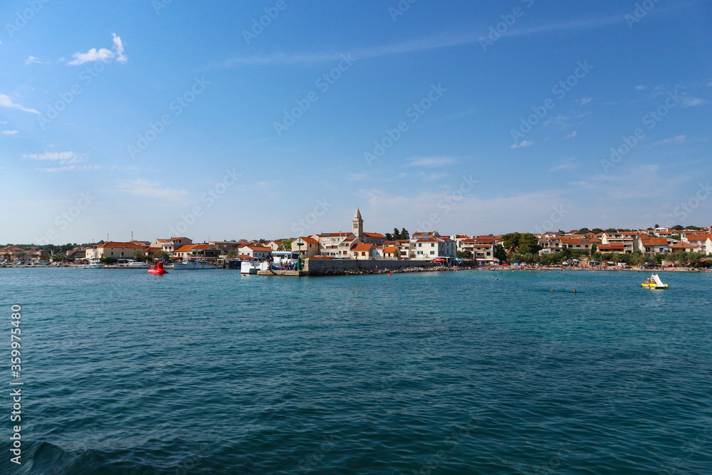 Town of Pakostane with its family houses and church tower on the shore, photographed from the boat